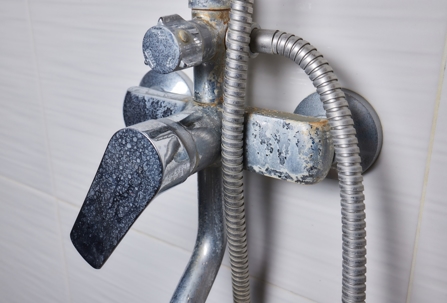 Close-up of a shower faucet and metal hose covered with white limescale buildup and water stains caused by hard water.